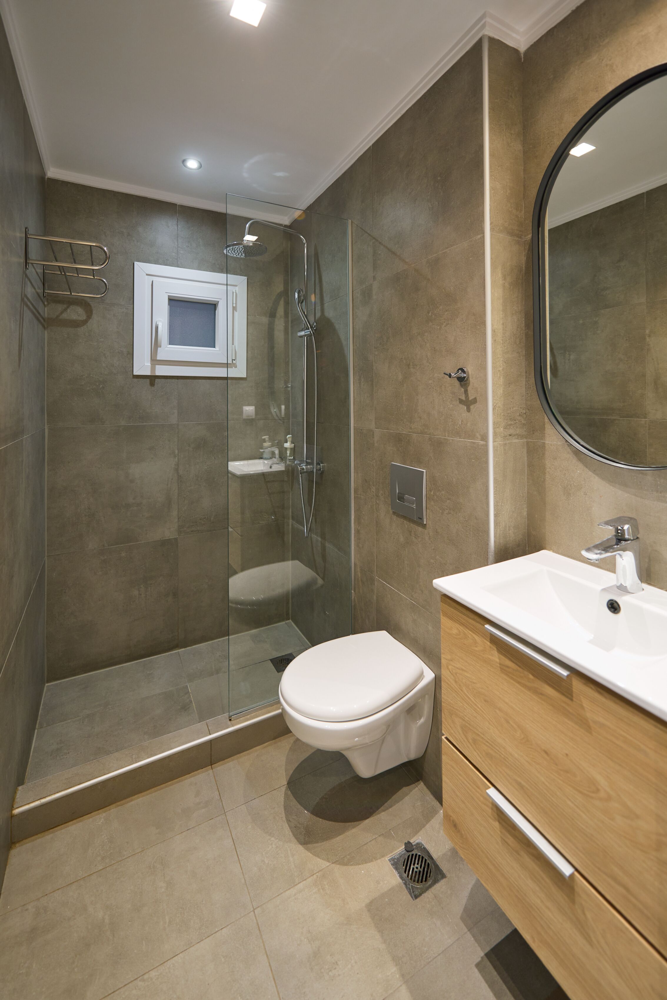 Un baño moderno con ducha envuelta en vidrio, inodoro blanco y tocador de madera con espejo.