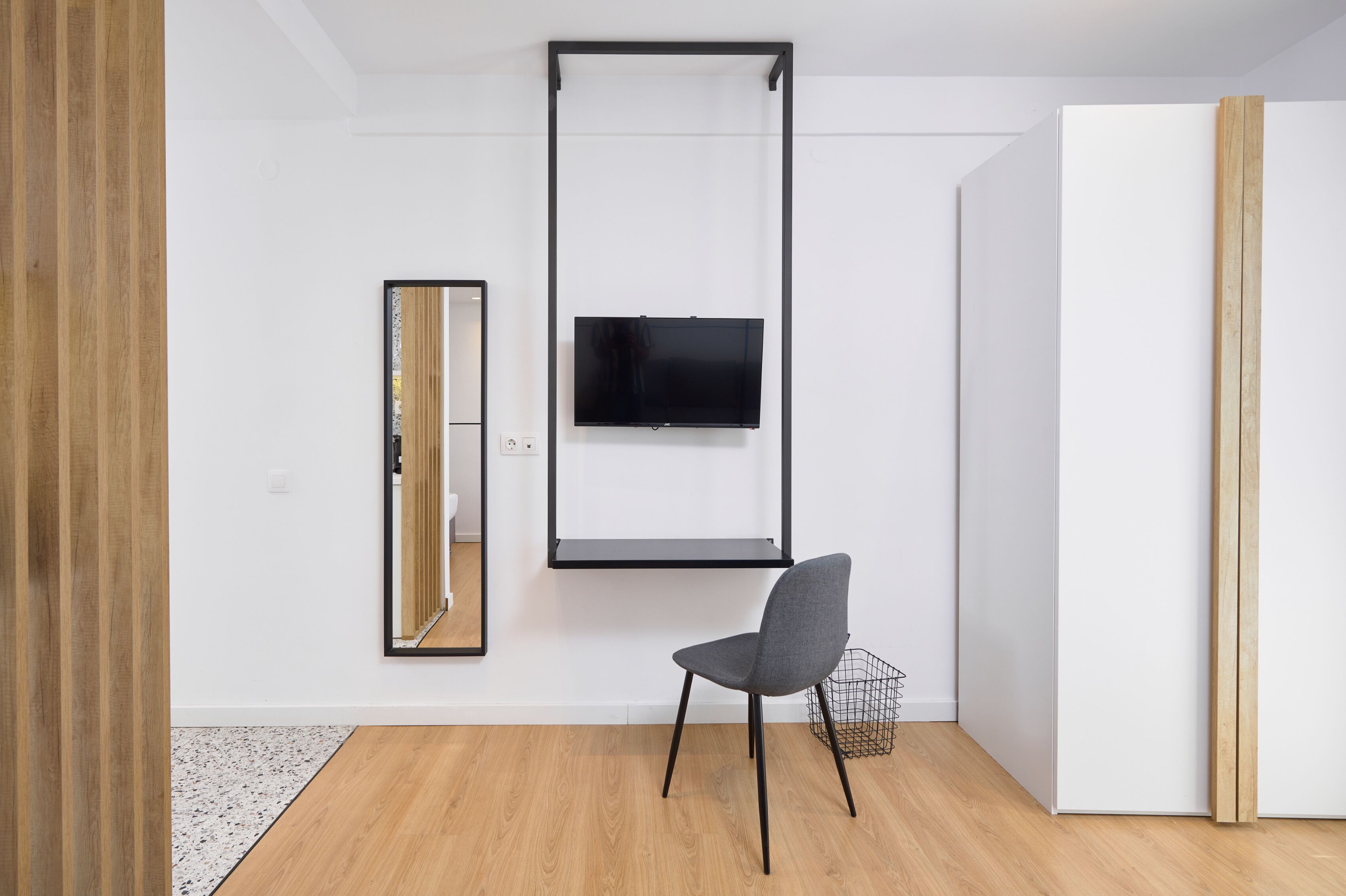 A modern room with a flat-screen TV mounted on the wall, a chair, and a wooden floor.