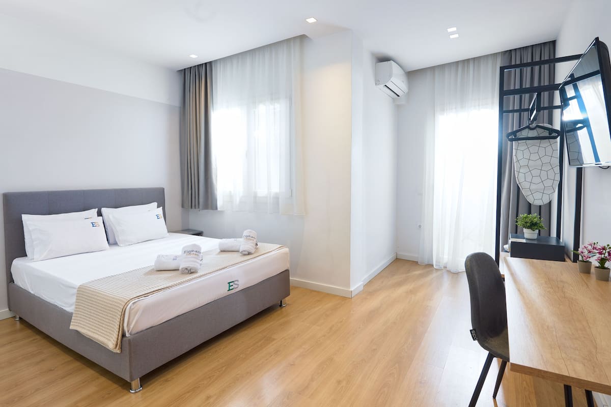 Moderni hotellihuone, jossa on sänky, puinen työpöytä ja vaateteline.
