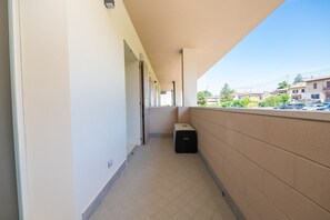 Un pasillo con piso de baldosas, un bote de basura y vistas a una calle residencial con coches estacionados y edificios.