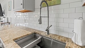 Eine Küche mit weißen, im Zickzackmuster angeordneten Fliesen, einer Arbeitsplatte aus Granit, einer Spüle aus Edelstahl und einem Handtuchhalter.