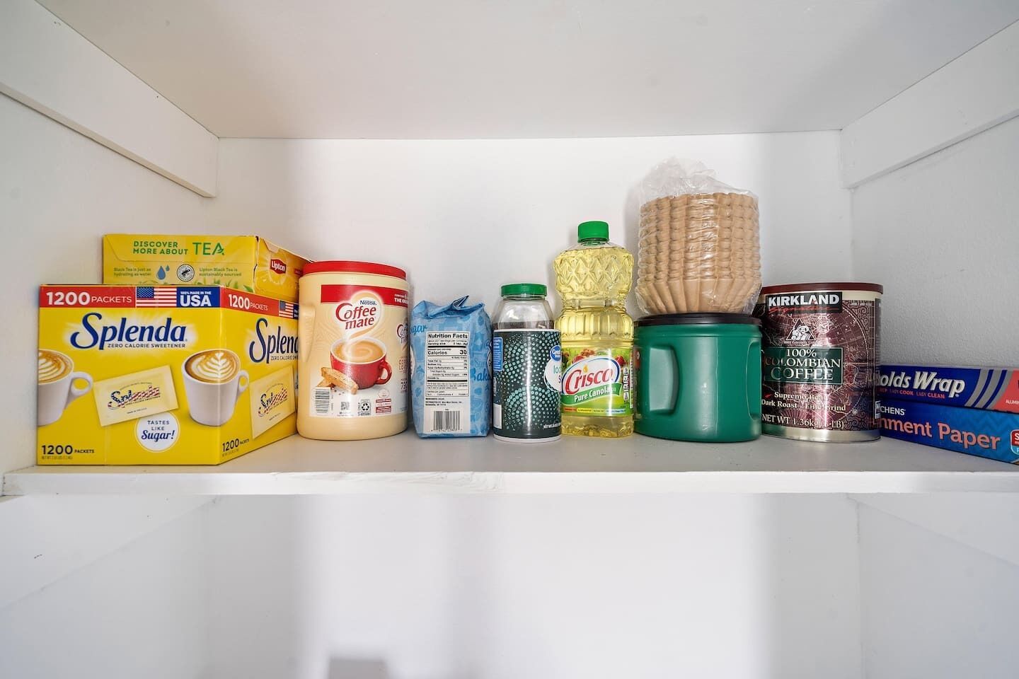 Scaffale del frigorifero con diversi prodotti alimentari, tra cui bustine di Splenda, caffè e salse.