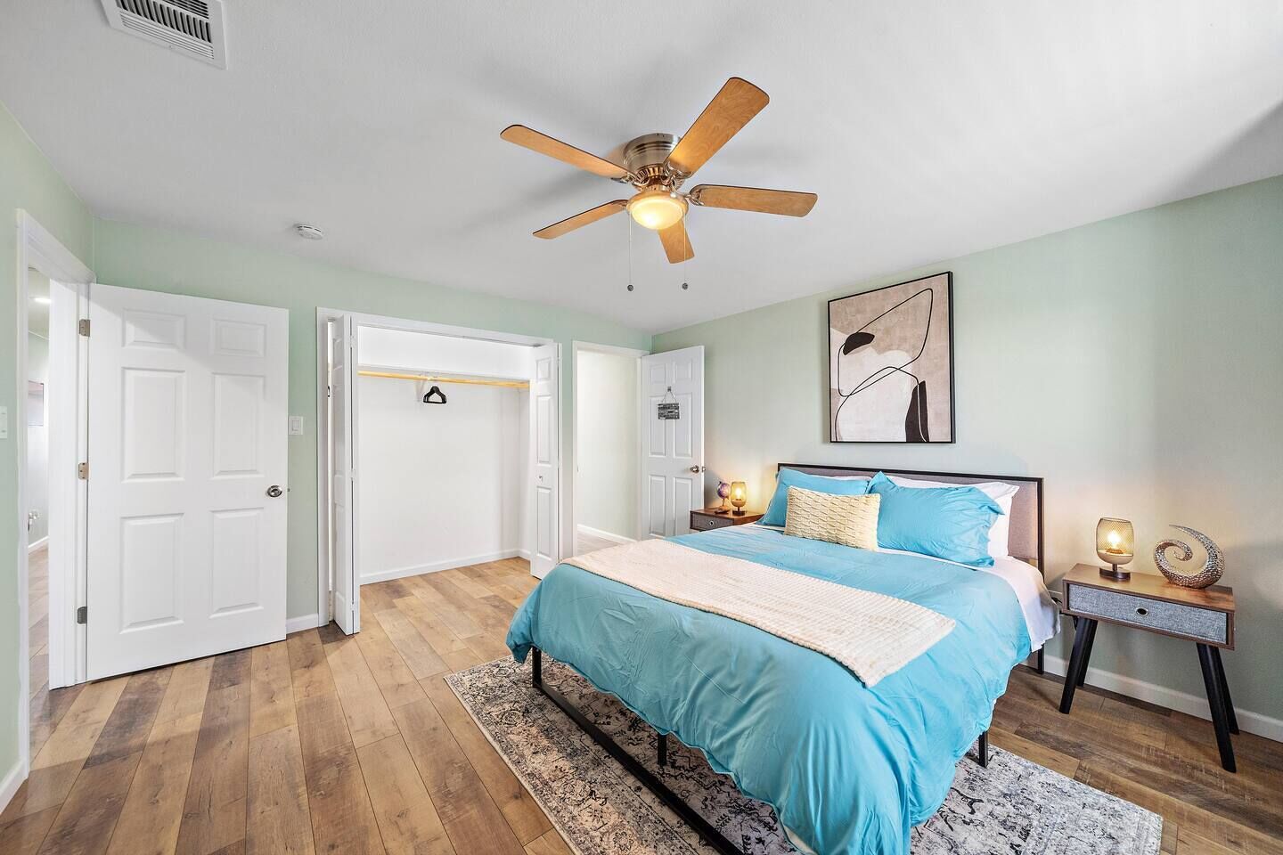 A bedroom with a bed, bedside tables, a ceiling fan, and a door to another room.
