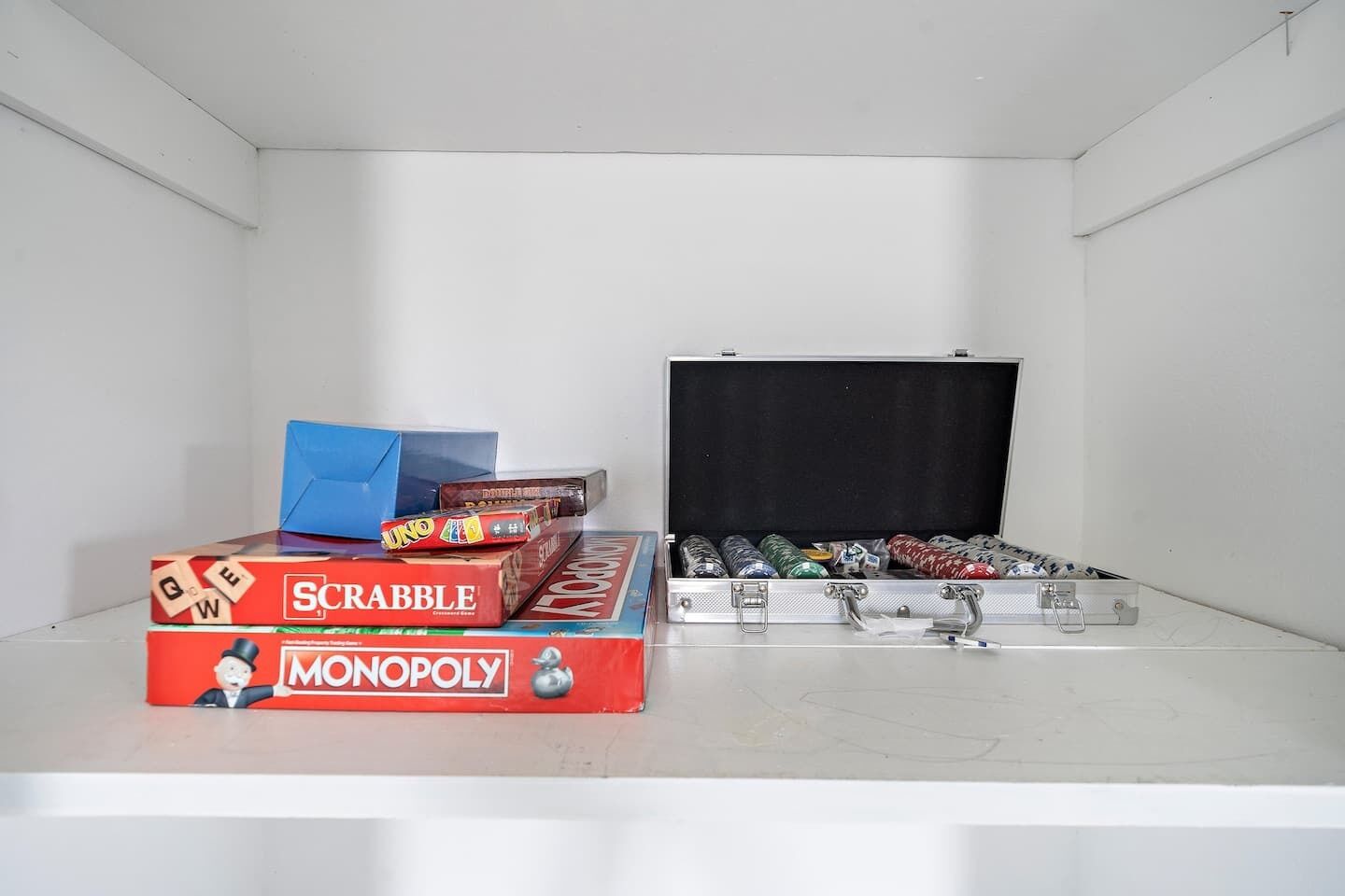 Um quarto com uma parede branca e um quadro negro grande. Há três jogos de tabuleiro: Scrabble, Monopoly e UNO.