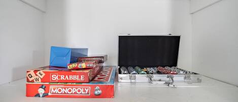 Um quarto com uma parede branca e um quadro negro grande. Há três jogos de tabuleiro: Scrabble, Monopoly e UNO.