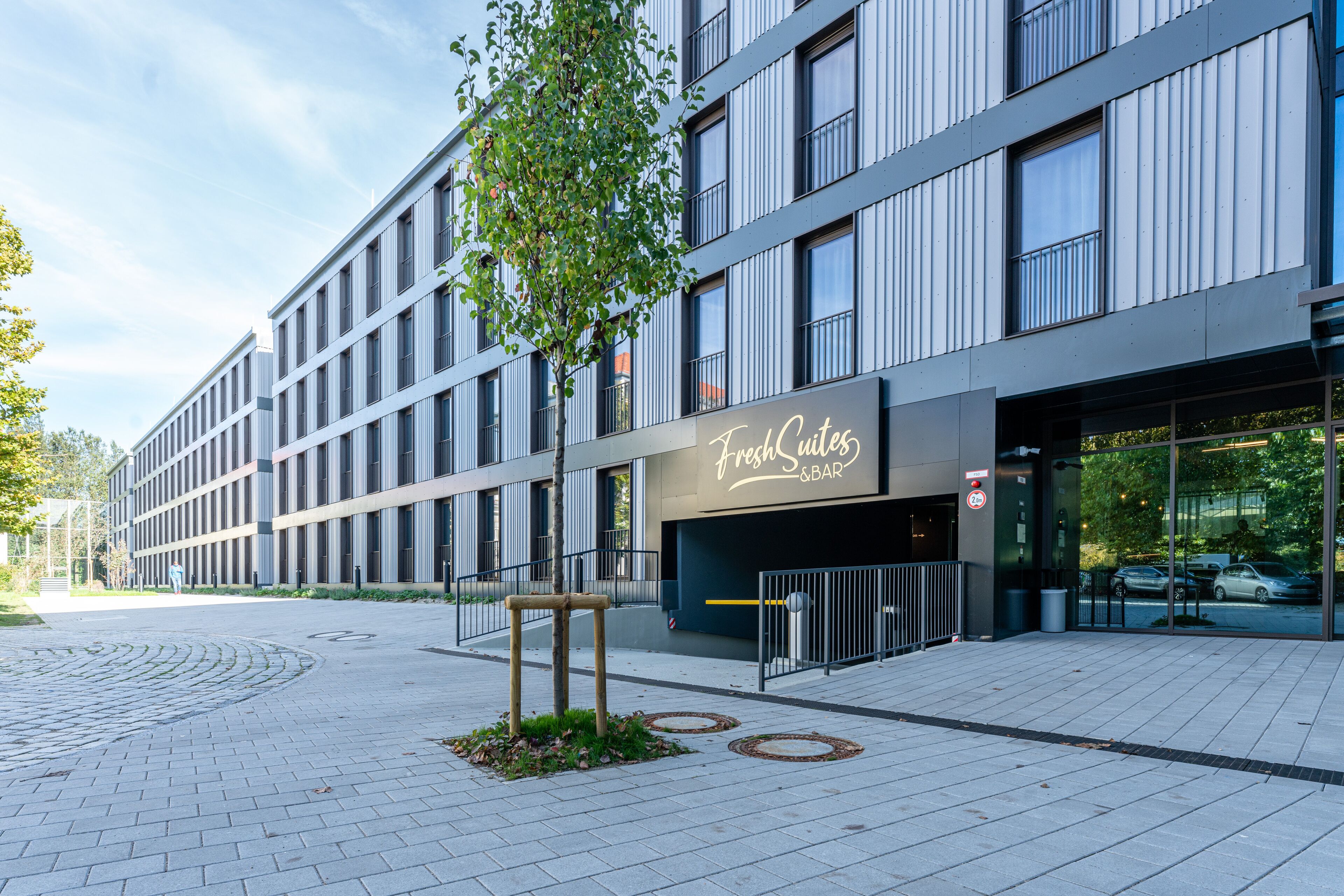 A modern building with a 'Fresh & Bar' sign, a paved walkway, and a tree.