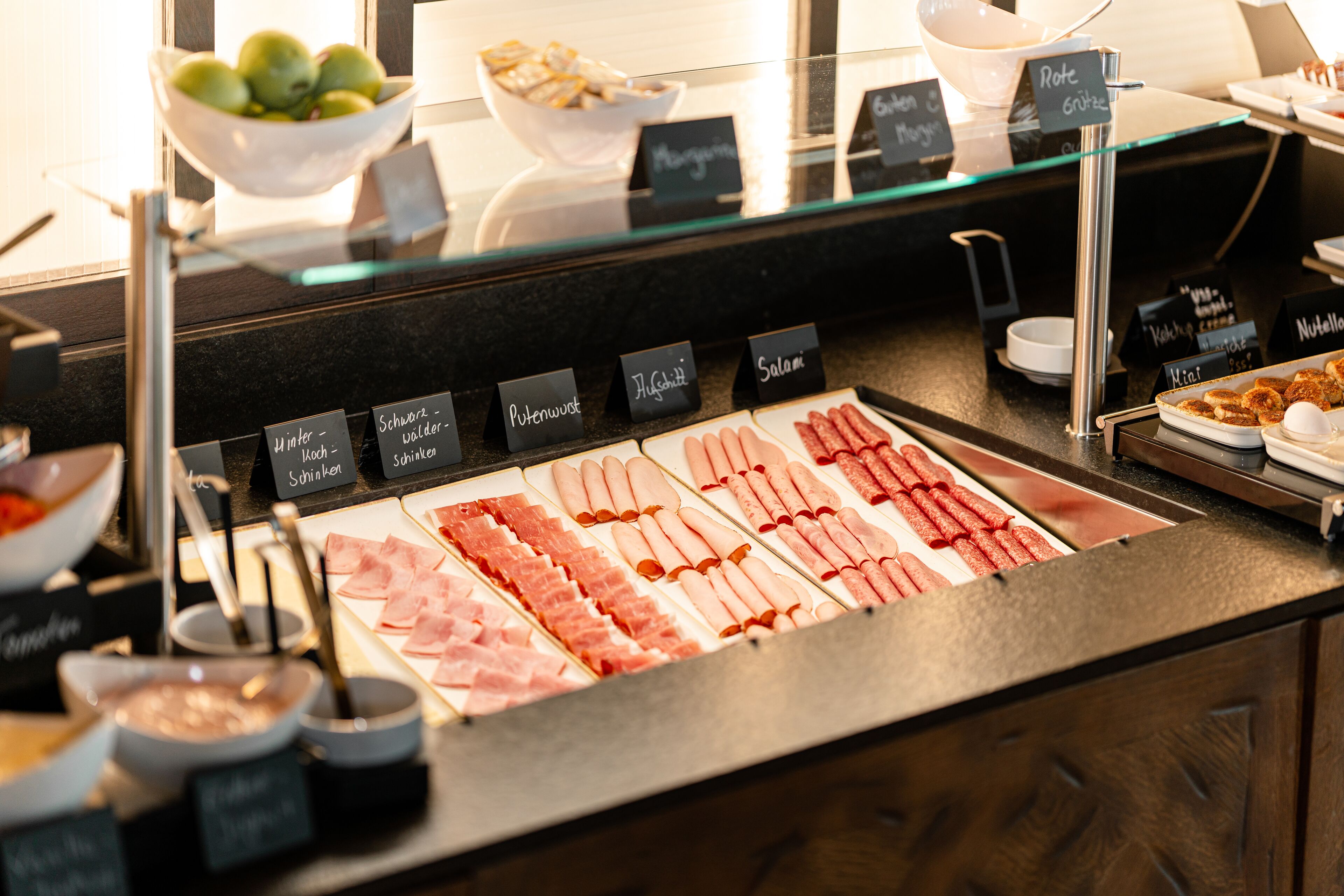 Mostrador de charcutería con diferentes carnes y un bol de frutas.