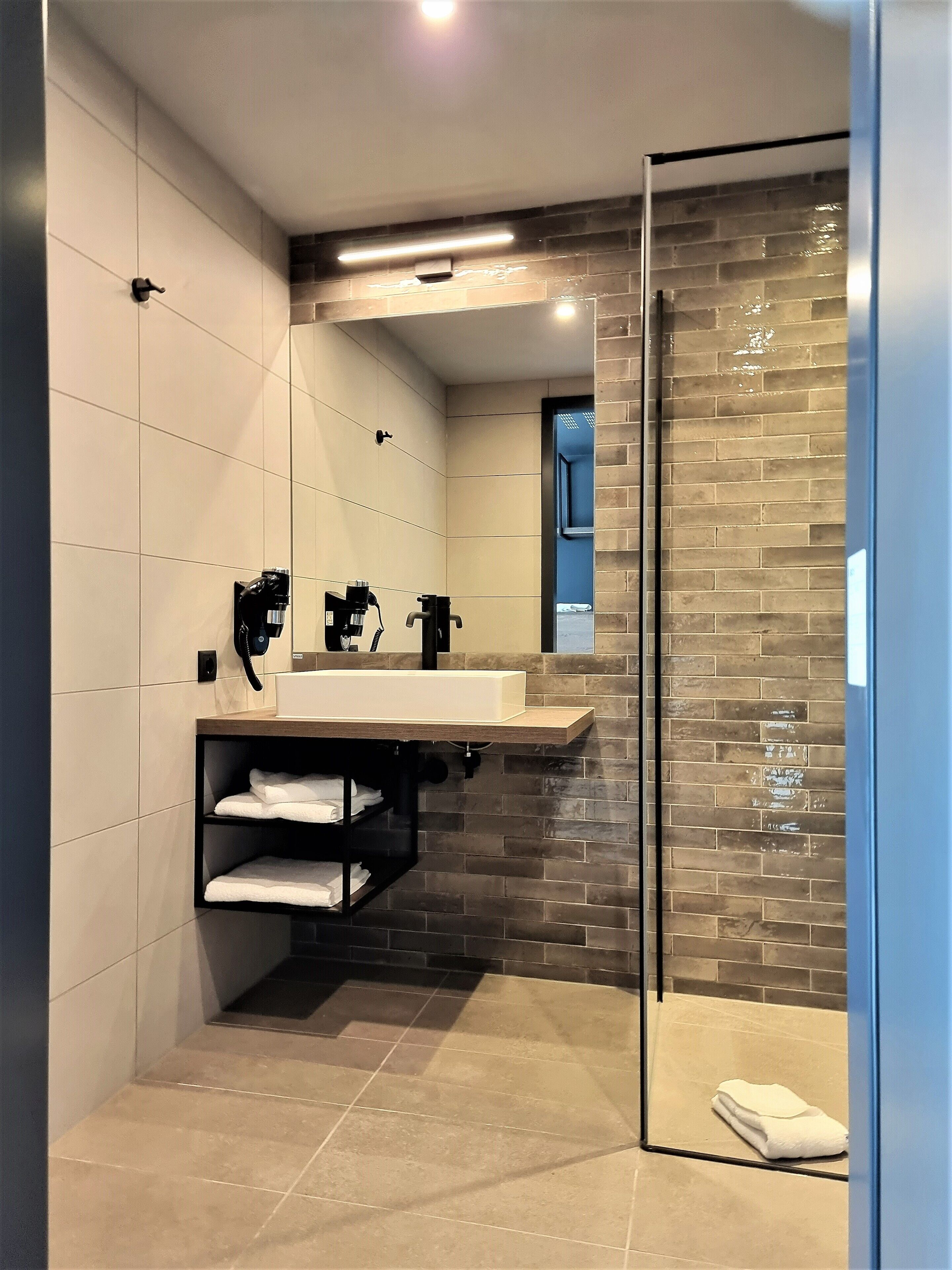 A modern bathroom with a glass shower enclosure, a white sink with a wooden countertop, and a towel rack.