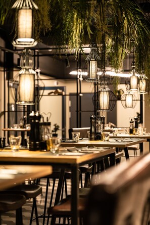 Un restaurante con mesas dispuestas para comer, lámparas colgantes de estilo farol y plantas.