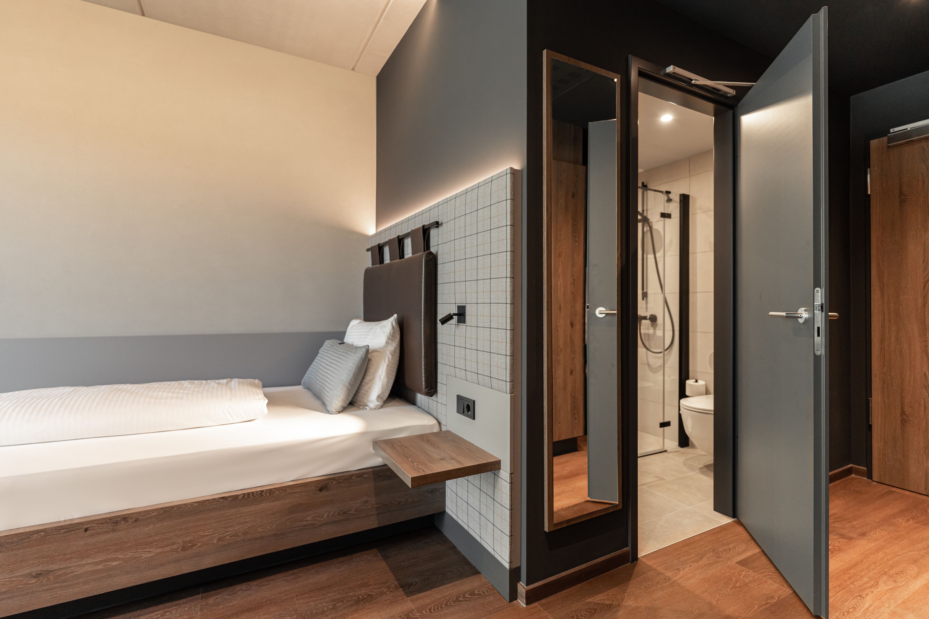 A modern bedroom with a bed, bedside table, and a view into the bathroom.