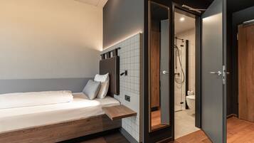 A modern bedroom with a bed, bedside table, and a view into the bathroom.