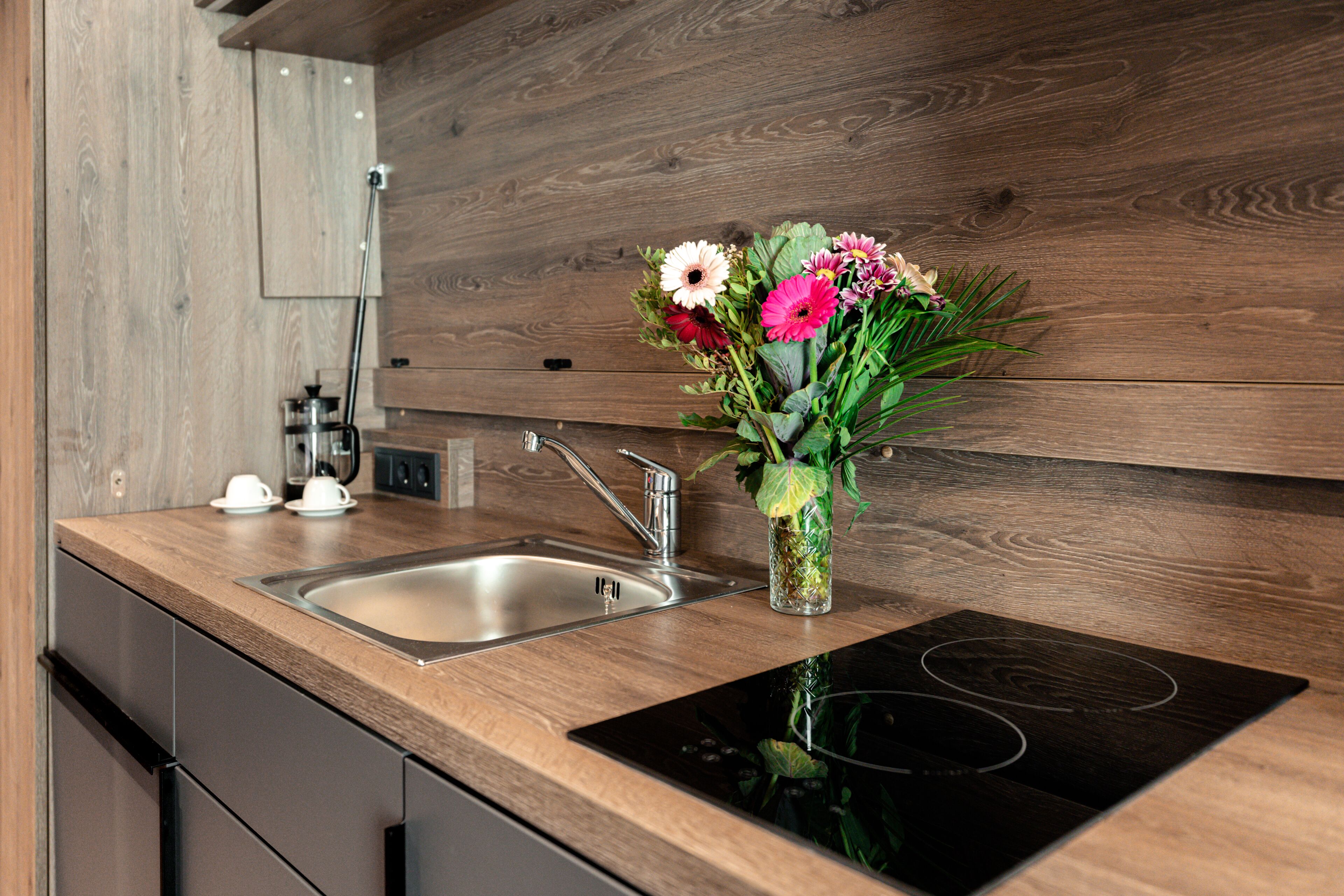 A modern kitchen with a wooden countertop, stainless steel sink, and an induction cooktop.