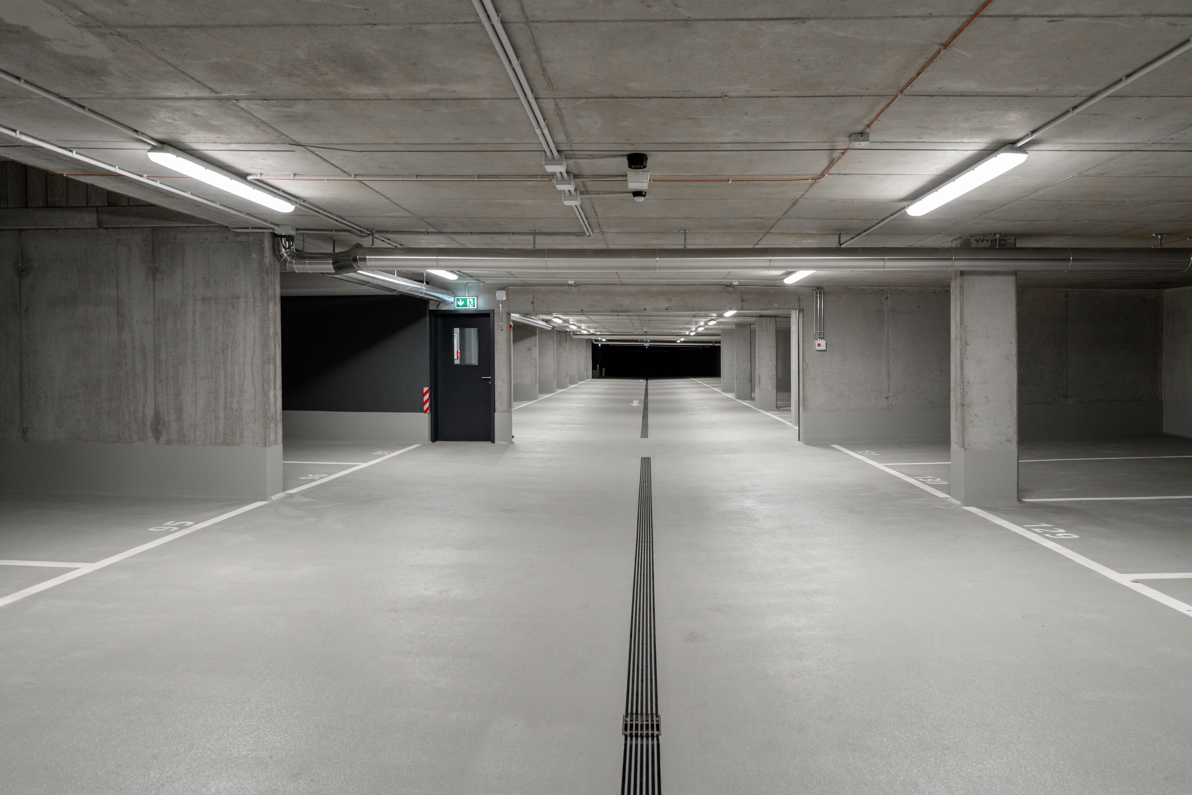 A long, empty parking garage with concrete pillars and fluorescent lighting.