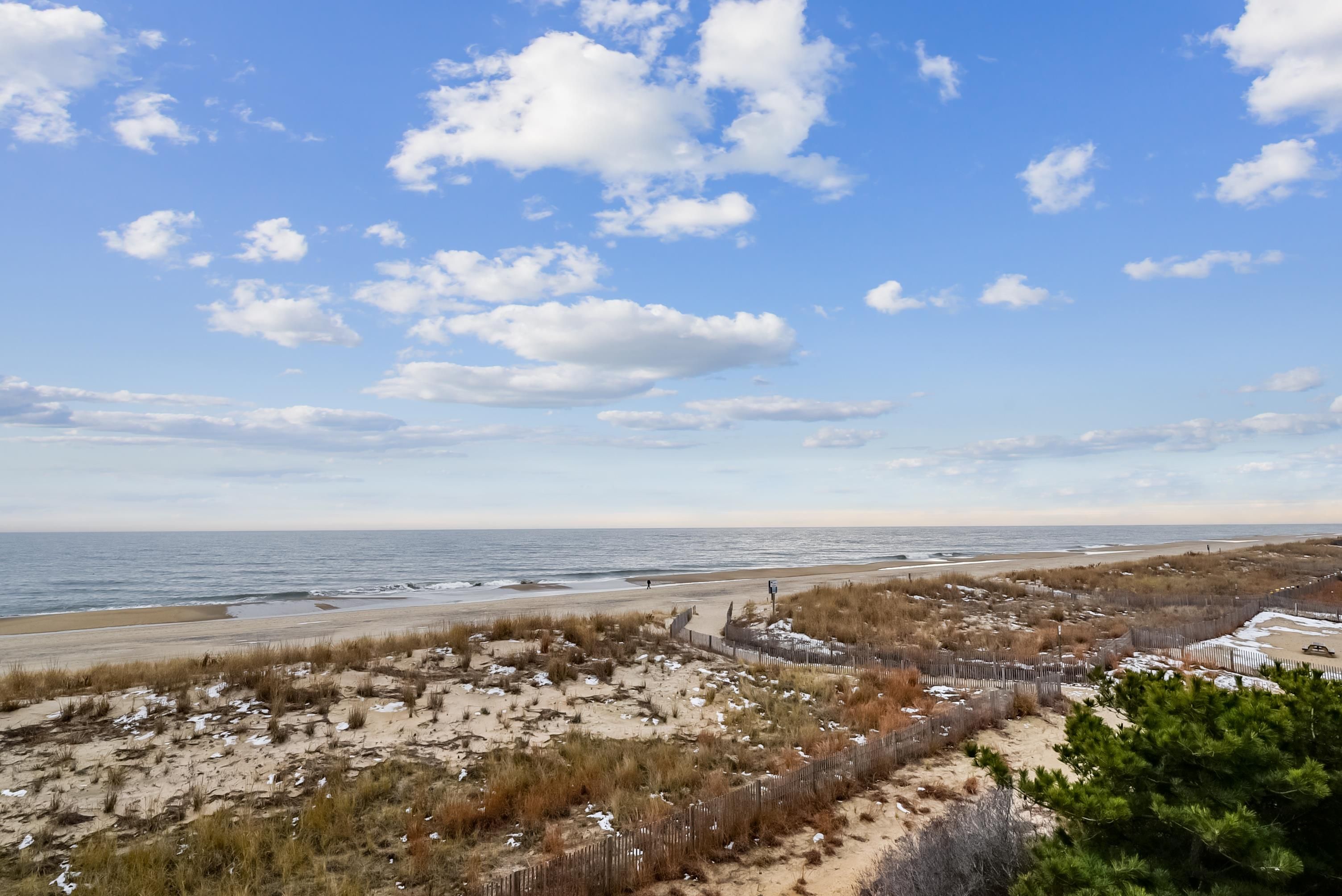 A beach with a wooden fence, sandy dunes, and a clear sky.