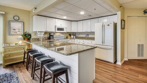 Una cocina con armarios blancos, encimera de granito y refrigerador.