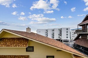 Un immeuble résidentiel doté d’un toit en pente, d’une cheminée bien visible et offrant une vue dégagée sur un grand complexe d’appartements en arrière-plan.
