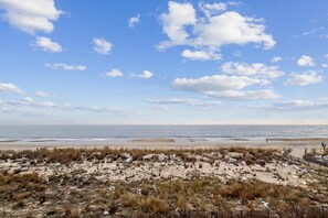 Een strand met een houten omheining, zandduinen en de oceaan op de achtergrond.