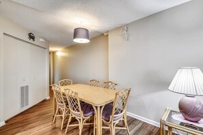 Un coin repas avec une table et des chaises en bois, un luminaire au plafond et une bouche d’aération fixée au mur.