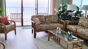 Uma sala de estar espaçosa com um sofá grande, uma mesa de centro e vista para o oceano através de amplas janelas.
