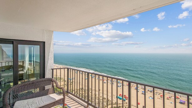 A balcony with a view of the ocean and beach, wicker furniture, and a railing. - XPLORIE ACTIVITIES & LINENS INCLUDED*! Plaza 3BR/2BA END UNIT with oceanfront & bayside balconies! (Ocean City)