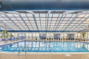 Une piscine intérieure à l’eau d’un bleu limpide, entourée de chaises longues et de plantes en pot.