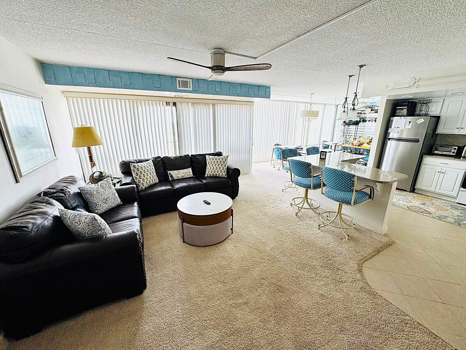 A living room with a black leather sofa, a round coffee table, and a dining area with blue chairs.