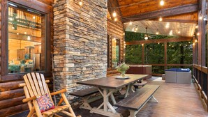 A wooden deck with a stone wall, wooden furniture, and string lights.