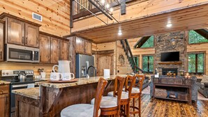 A spacious kitchen with wooden cabinets, a large island with bar stools, a built-in microwave, and a stone fireplace.