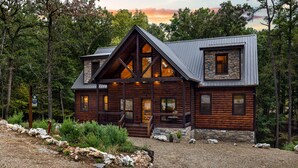 A log cabin with a stone foundation, large windows, and a porch.