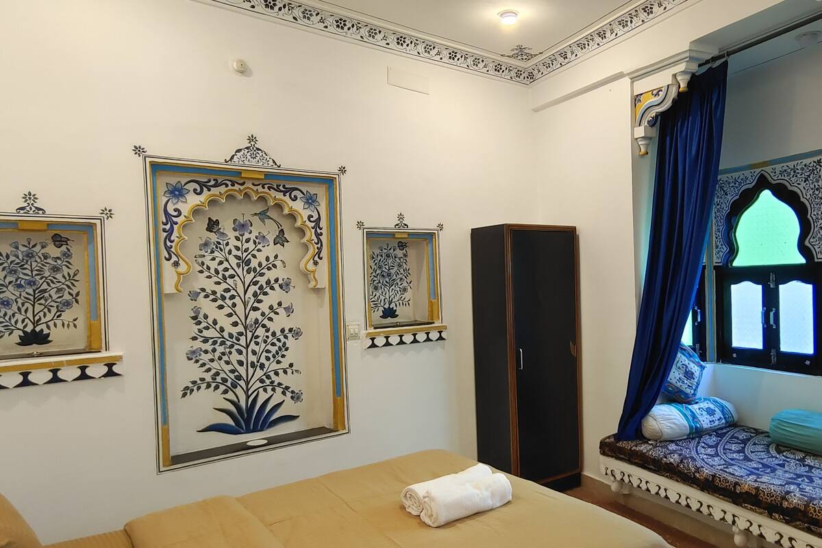 A room with a bed, a wardrobe, a window with blue curtains, and decorative wall art.