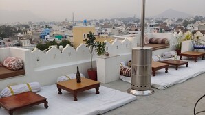 A rooftop terrace with seating, a table, a potted plant, and a solar heater. - The Rustic Monk (Udaipur)