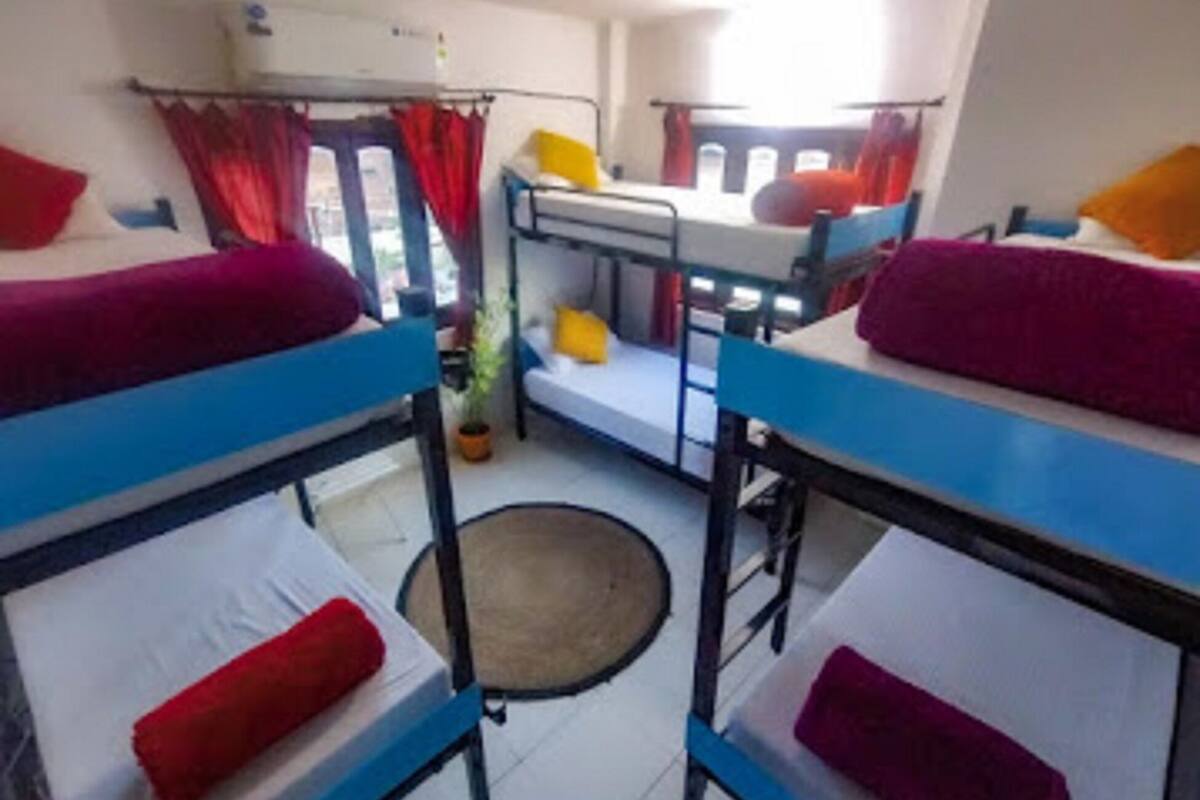 A dormitory room with bunk beds, a small table, and a window with curtains.