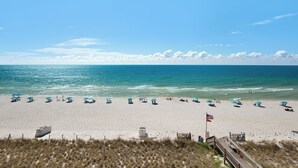 A beach with rows of blue umbrellas and beach chairs, a lifeguard tower, and a wooden boardwalk leading to the water.