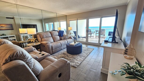 A modern living room with a large sofa, a coffee table, and a view of the ocean through large sliding doors. - Sandy Key 438: 3 BR/2 BA Beachfront Condo, Perdido Key, FL. On-Site Rental Office, Sleeps 8 (Pensacola)