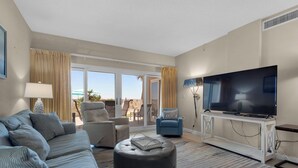 Ein Hotelzimmer mit Sofa, Hocker, Sesseln, einem Fernseher und Blick ins Freie.