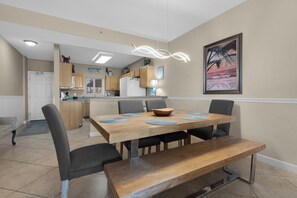 A dining area with a wooden table, four chairs, and a bench. There is a kitchen in the background with wooden cabinets and a refrigerator. - Sandy Key 136: 2 BR/2 BA Beachfront in Perdido Key, FL On-Site Rental Office Sleeps 6 (Pensacola)