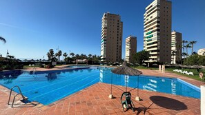 A swimming pool with a tiled deck, lounge chairs, and umbrellas. - Apartment in Playamar I in Torremolinos (Torremolinos)