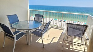 Varanda com mesa e cadeiras de vidro, com vista para a praia e o oceano.