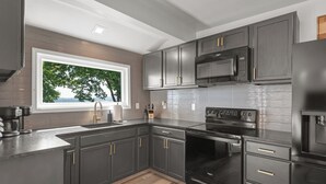 Una cocina moderna con armarios oscuros, microondas integrado y un ventanal con vistas a árboles.