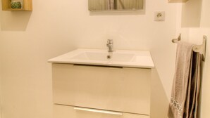 A bathroom with a white sink, wooden shelves, and a mirror. - Gite Le Mistral 2/4 persons 6kms from the puy du fou park (Mallièvre)