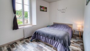 A bedroom with a bed, a window with curtains, a radiator, a wall decoration, and a bedside table with a lamp. - Gite Le Mistral 2/4 persons 6kms from the puy du fou park (Mallièvre)