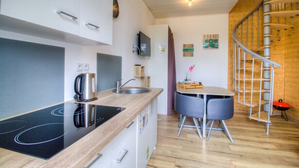 A modern kitchen with an induction cooktop, a sink, and a dining area with a small table and chairs. - Gite Le Mistral 2/4 persons 6kms from the puy du fou park (Mallièvre)