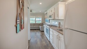 A kitchen with white cabinets, a stove, and a refrigerator. There is a window with blinds and a ceiling fan. - Pet-Friendly Cottage in Amenity-Filled Currituck Sound Campground (J04) (Coinjock)