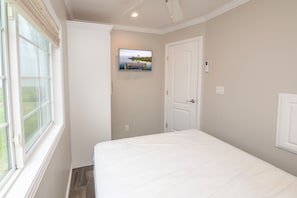 A bedroom with a bed, a window, a door, and a wall-mounted TV.