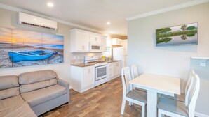 A modern kitchen with white cabinets, a microwave, and a stove. There is a dining area with a white table and chairs. - Waterview Cabin on Currituck Sound - Great Campground Amenities (WV90) (Coinjock)