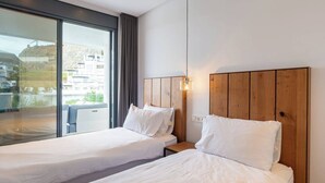 A hotel room with two single beds, a wooden headboard, a bedside table, and a large window offering a view of buildings and greenery. - La Quinta 3 bedroom apartment with Private Hot Tub (Benahavís)