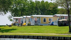 Une rangée de maisons mobiles, avec une pelouse devant, un quai et une étendue d’eau en arrière-plan.