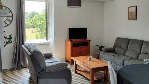 A living room with a sofa, a television, a coffee table, and a patterned floor. - Charming house on the banks of the Louet (Mûrs-Erigné)