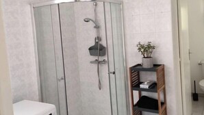 A modern bathroom with a glass-enclosed shower, a built-in washing machine, and a wooden shelf with toiletries. - Charming house on the banks of the Louet (Mûrs-Erigné)