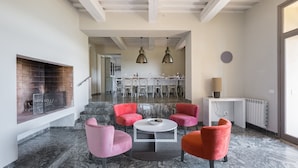 Un salon moderne avec une cheminée, des fauteuils rouges, un sol en marbre et, au fond, un coin repas.